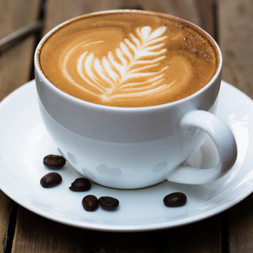 Ein zubereiteter Cappuccino hübsch in Scene gesetzt und mit Kaffeebohnen auf dem Teller als Dekorationselement.