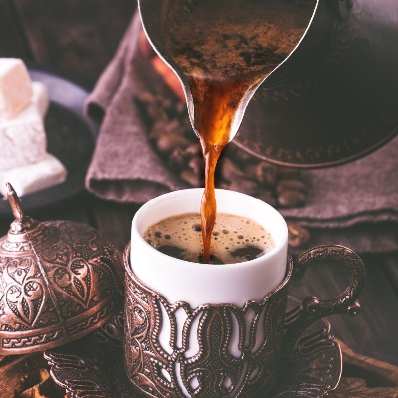 Dieses Bild zeigt eine Kanne und Tasse mit Mokka Kaffee, während die Kanne eingießt.